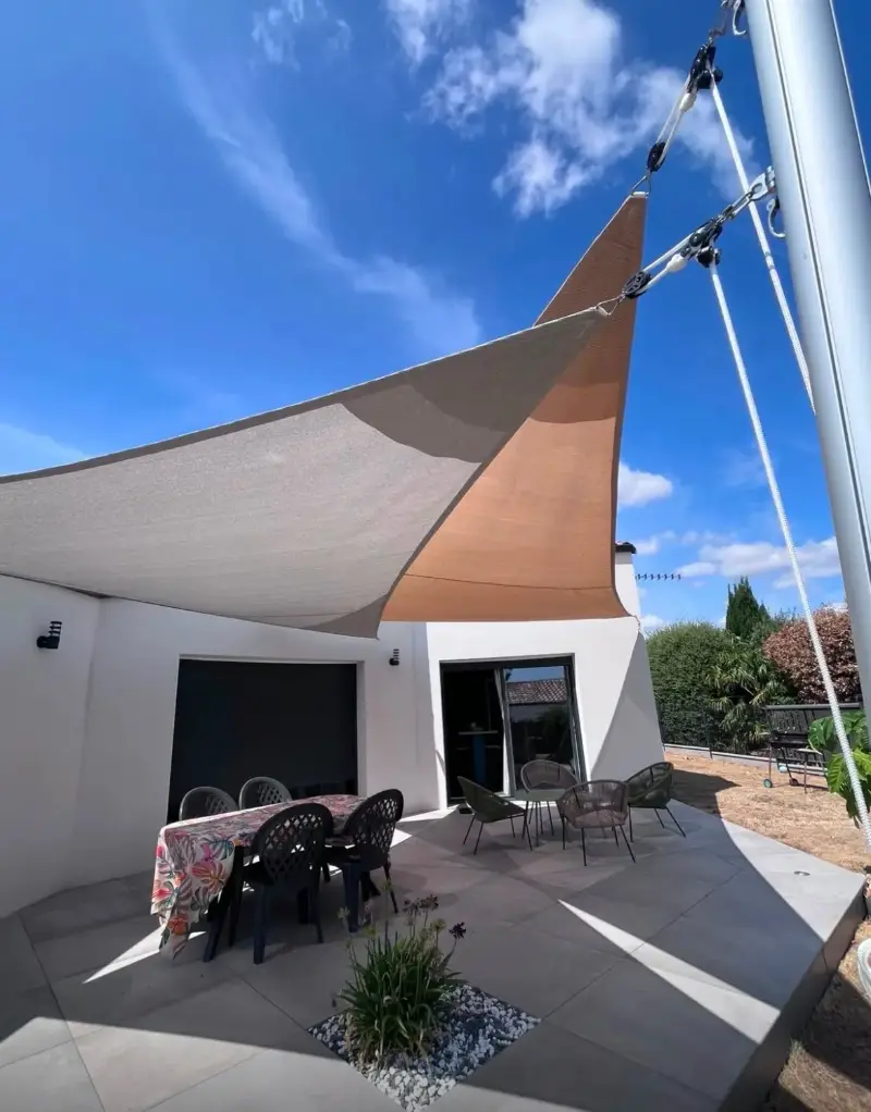 Voiles d’ombrage grise et orange superposées au-dessus de la terrasse d’une maison