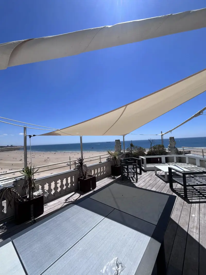 Voiles d’ombrage écrues tendues sur un toit-terrasse face à la plage et à l’océan