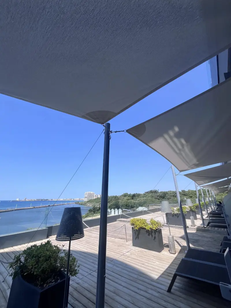 Voiles d’ombrage grises tendues au-dessus d’un toit-terrasse en bois face à la mer